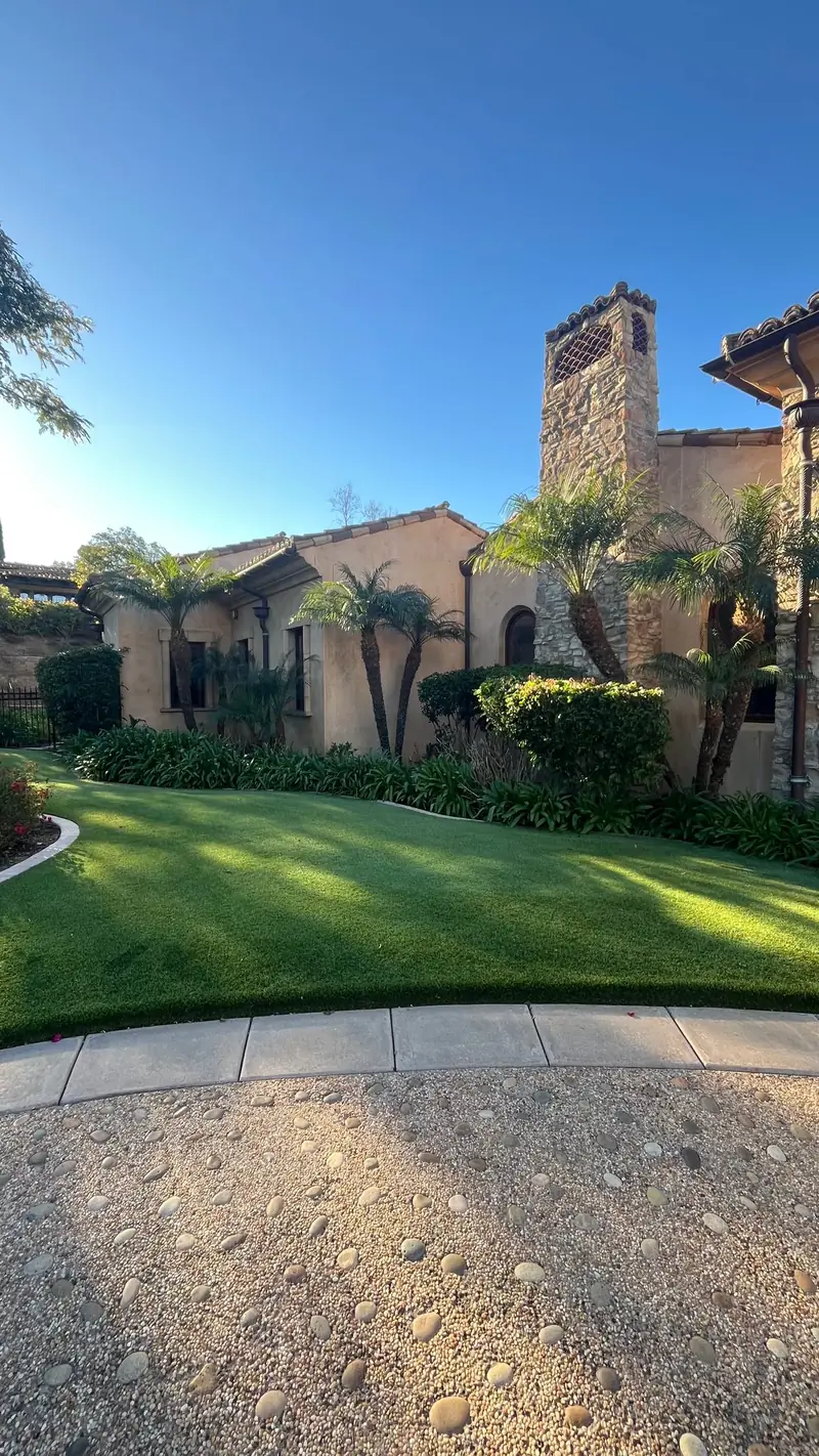 A green lawn and palms below a stone chimney