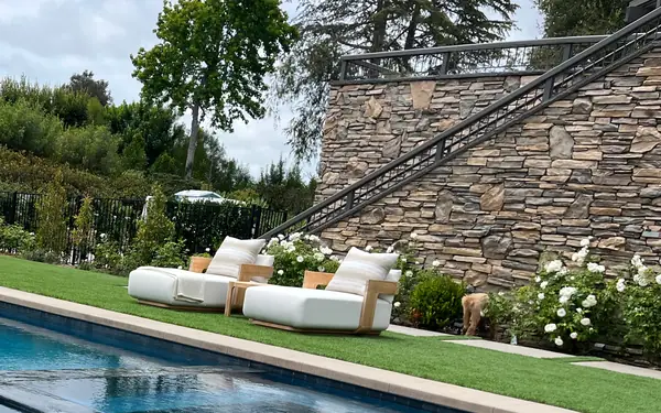 A long pool set in lawn, with white lounges and a stacked stone stair