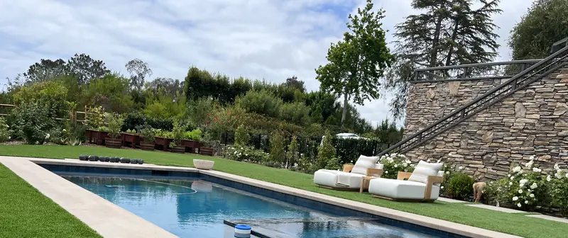 A long pool set in lawn, with white lounges and a stacked stone stair